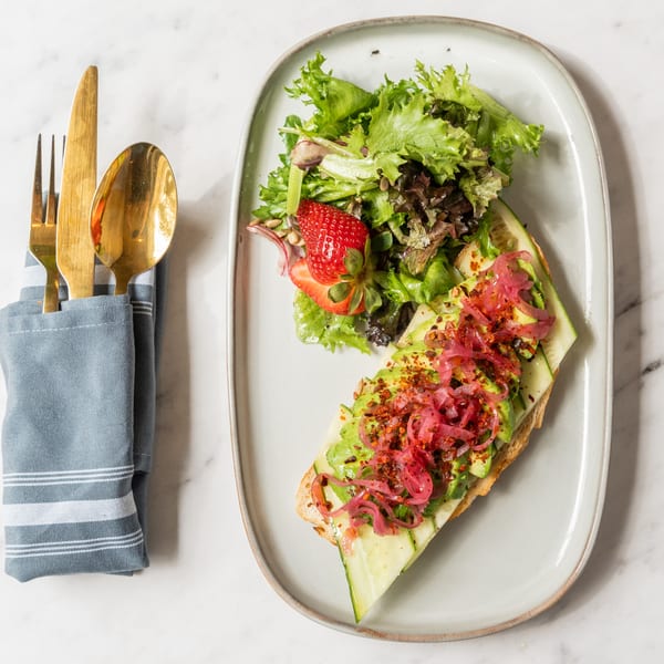 Avocado toast with pickled onions and chili flakes, served with a side salad and strawberry.