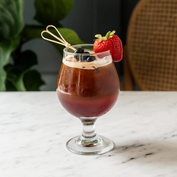 A Café Taureau iced coffee drink, garnished with blueberries and a strawberry, on a marble table.