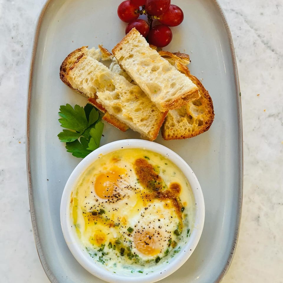 Baked eggs with herbs and cheese, served with toasted bread and red grapes on a light plate.