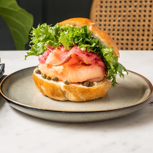 Café Taureau's salmon sandwich with lettuce, pickled onions, cream cheese, and capers on a bun.