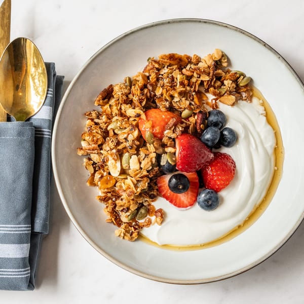 Granola with yogurt, strawberries, blueberries, and honey in a white bowl with a gold spoon.